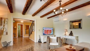Amplia sala de estar con techo de madera, televisor, mobiliario de mimbre y una escalera que conduce a otra habitación.