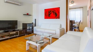 En moderne stue med et fladskærms-tv, hvide sofaer, et glas-sofabord og et rødt abstrakt billede på væggen.