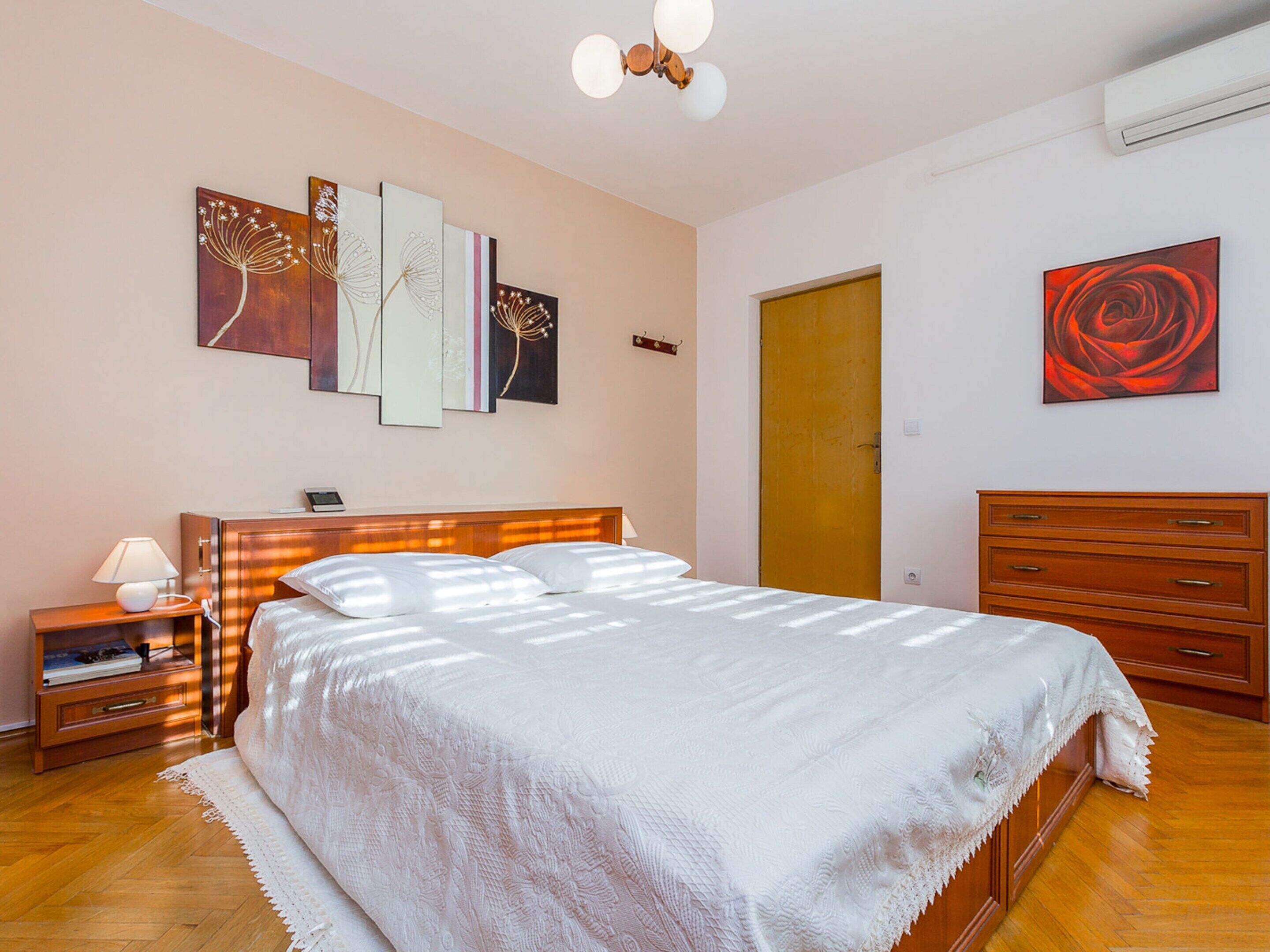 A bedroom with a bed, bedside table, lamp, dresser, and artwork on the walls.