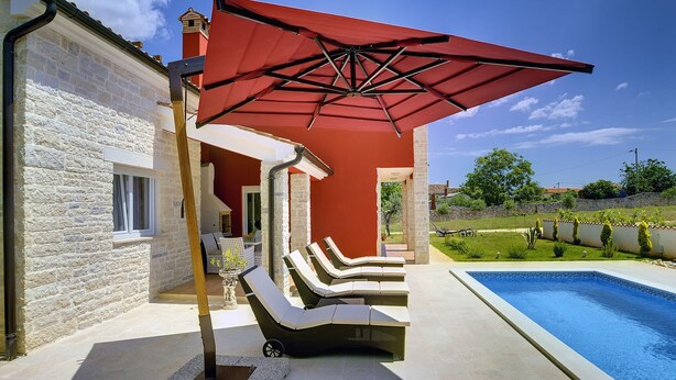 A poolside area with a red umbrella, lounge chairs, and a stone building. - Villa in Bratulici With Pool Near Beach (Marcana)