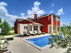 Ein zweistöckiges Haus mit Swimmingpool, Außenbereich mit Sitzgelegenheiten und roter Fassade.