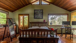 A bedroom with a wooden ceiling, a bed, a desk with a computer, and a window with a view of trees. - The Getaway Perth Hills (Roleystone)