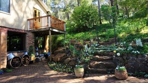 A house with a wooden balcony, a brick entrance, and a garden with various plants and flowers. - The Getaway Perth Hills (Roleystone)