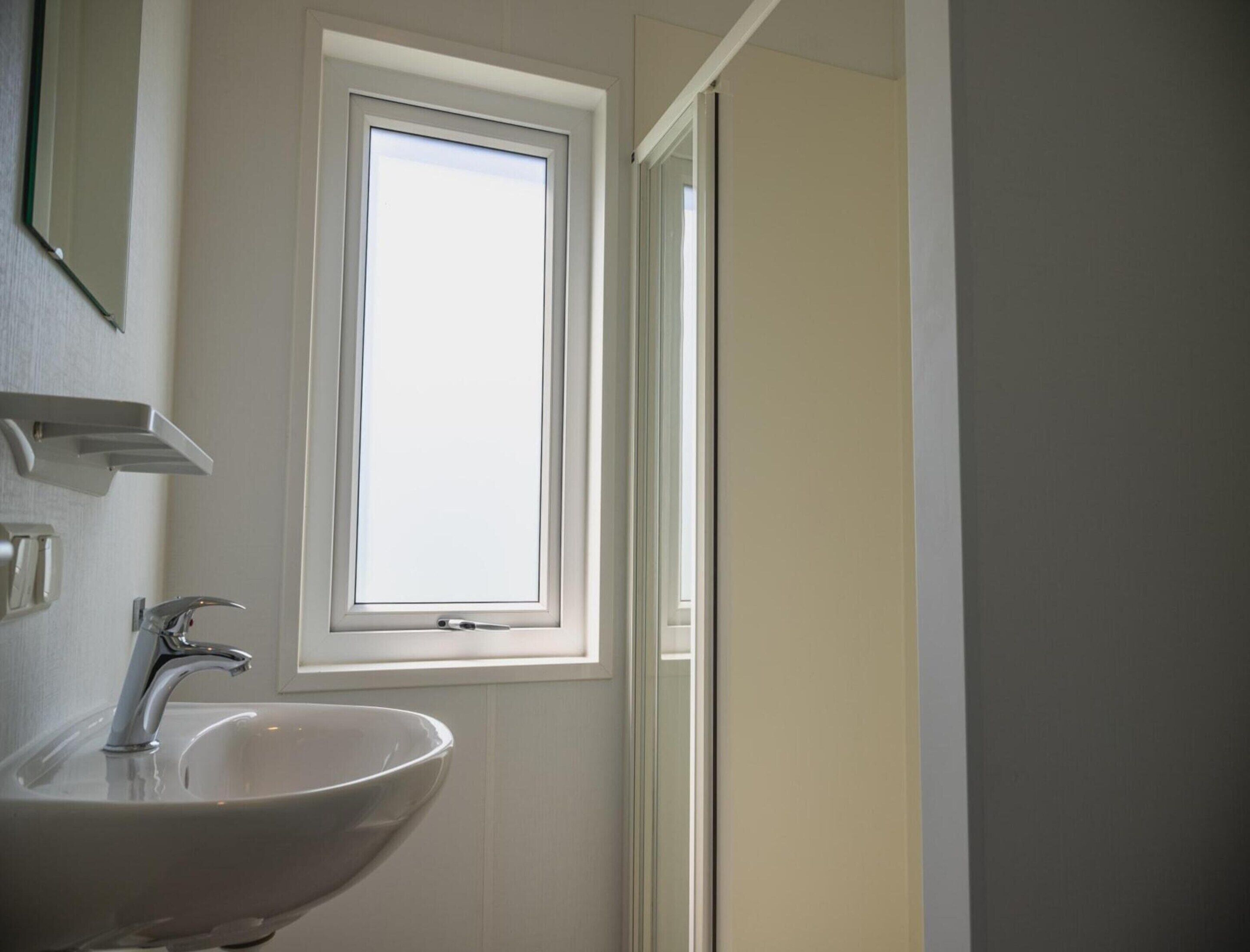 A bathroom with a white sink, a mirror, and a window.