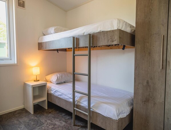 Dormitorio con literas, una mesita de noche con lámpara y un armario.