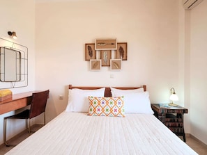 A neatly arranged bedroom with a bed, a desk, a chair, and a bedside table with a lamp.