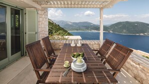 A wooden table with chairs and a view of the sea and mountains. - Luxurious Villa in Vasiliki with Swimming Pool & Hot Tub (Lefkada)