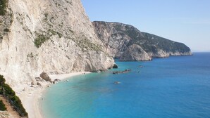 A coastal landscape with a steep cliff, a sandy beach, and clear blue waters. - Luxurious Villa in Vasiliki with Swimming Pool & Hot Tub (Lefkada)