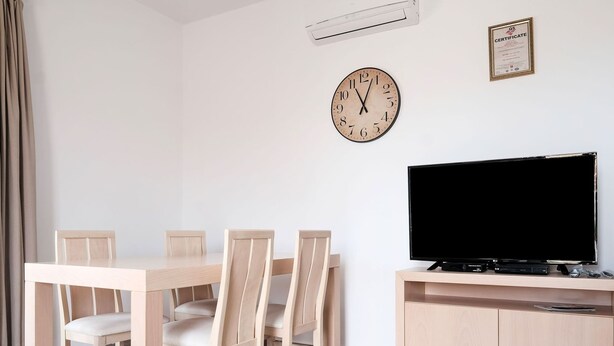 A dining area with a wooden table and chairs, a television on a cabinet, and a wall clock. - Sun-kissed Villa in Latsimas With Pool (Mylopotamos)