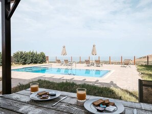 Vista da piscina com céu claro, cadeiras de descanso e uma mesa com comida e bebidas.