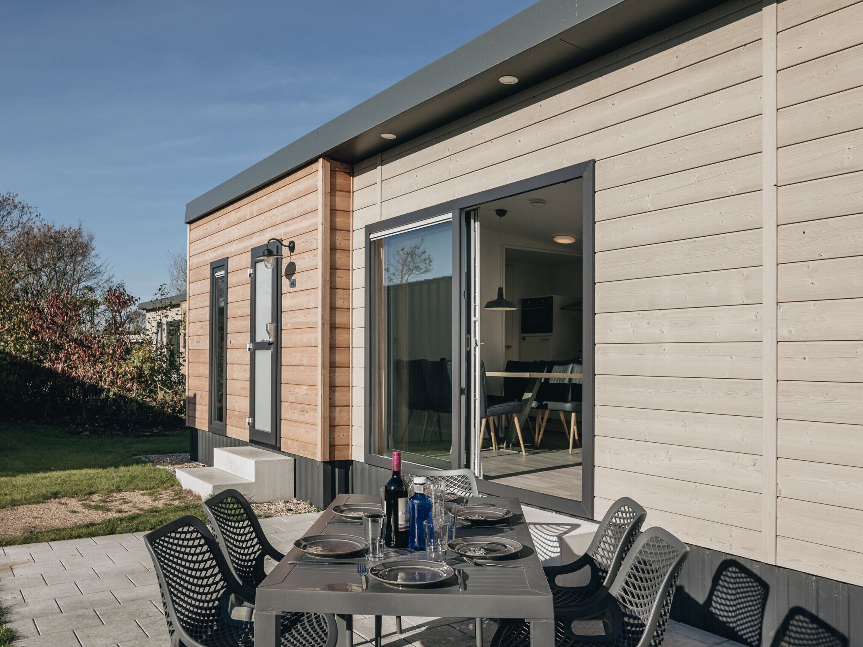 Un espace extérieur aménagé pour les repas, avec une table dressée pour quatre personnes, entourée de chaises, et une porte-fenêtre coulissante donnant sur un espace intérieur.