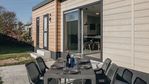 An outdoor dining area with a table set for four, surrounded by chairs, and a sliding glass door leading to an interior space. - Modern Chalet With Dishwasher, Cosy Domburg Nearby (Domburg)