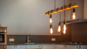 Una cocina moderna con una mesa y sillas de madera, un lámpara colgante con bombillas expuestas y un horno de acero inoxidable.