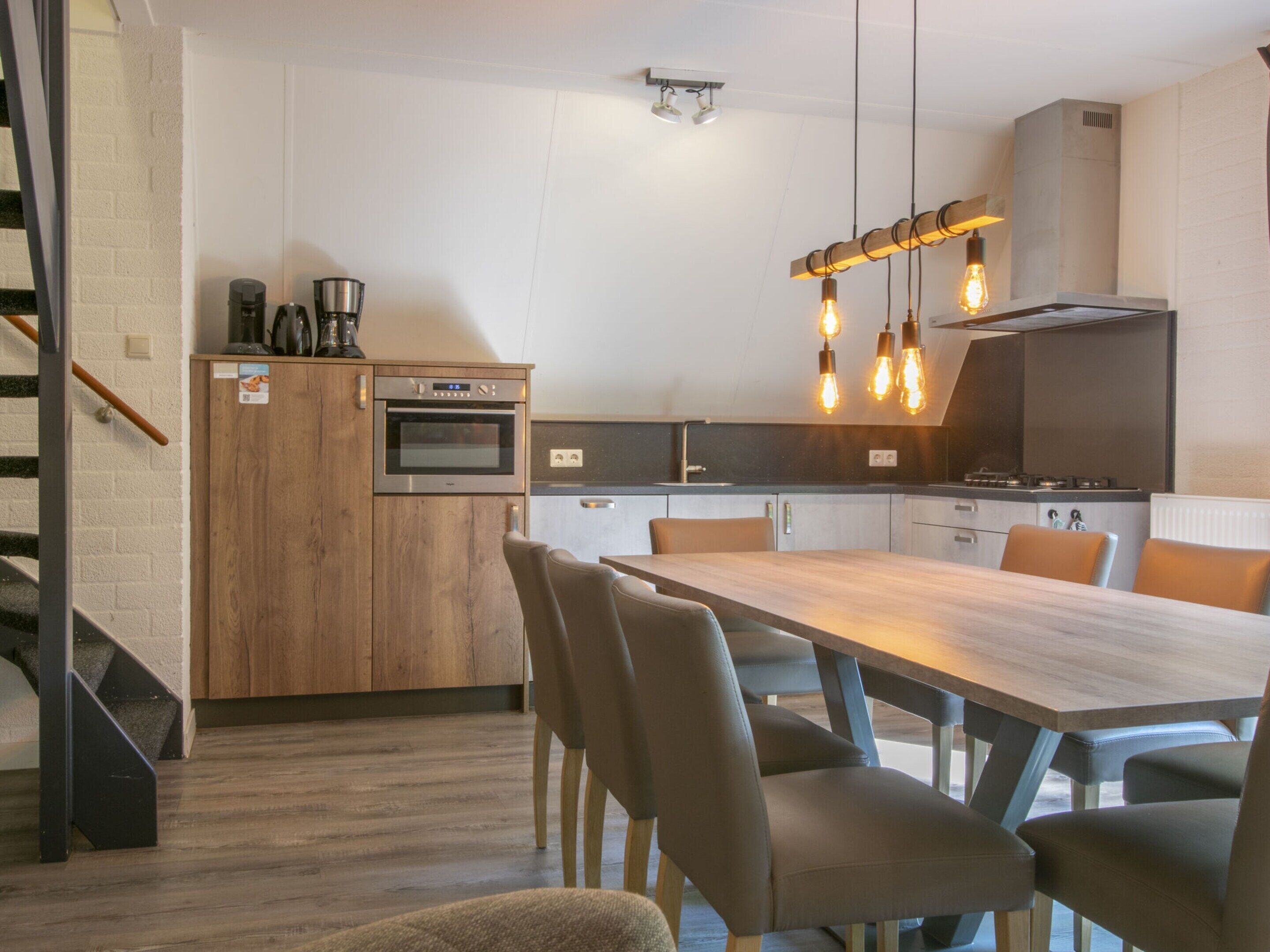 Une cuisine moderne avec des meubles en bois, un four encastré et un coin repas comprenant une longue table et des chaises.