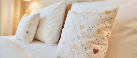 Una cama con sábanas blancas y almohadones decorativos con motivos de corazones y anillos.