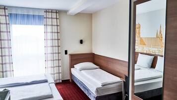 A hotel room with two beds, a red carpet, a window with curtains, and a mirror reflecting a building.