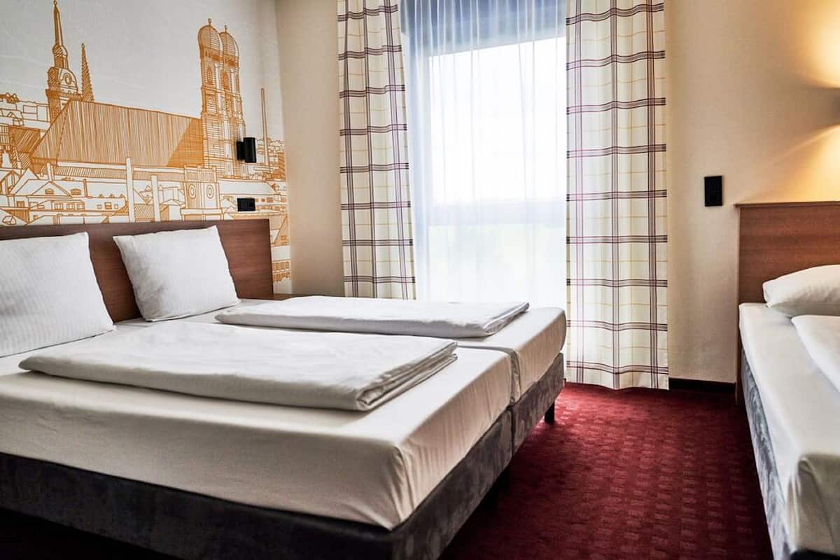 Habitación de hotel con dos camas, alfombra roja, un mural con vista a la ciudad y cortinas a cuadros.
