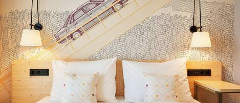 A bed with white bedding and patterned pillows, a wooden headboard, and a wall with a train illustration.