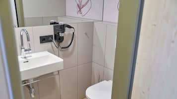 A small, modern bathroom with a white sink, a toilet, and a shower head mounted on the wall.