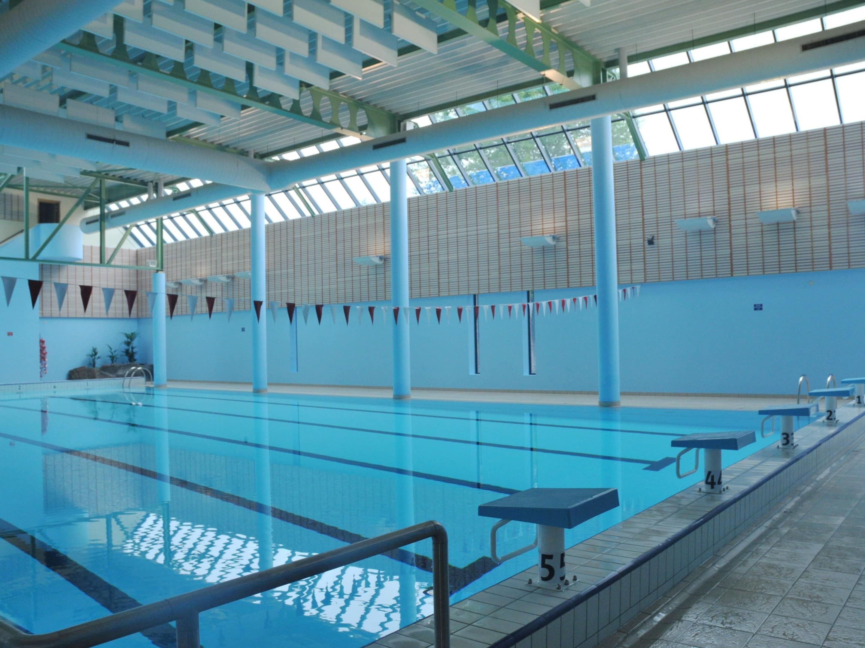 An indoor swimming pool with clear lanes, diving platforms, and a tiled floor.