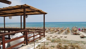 Ein Strandbereich mit einer Holzpergola, Liegestühlen und Sonnenschirmen.