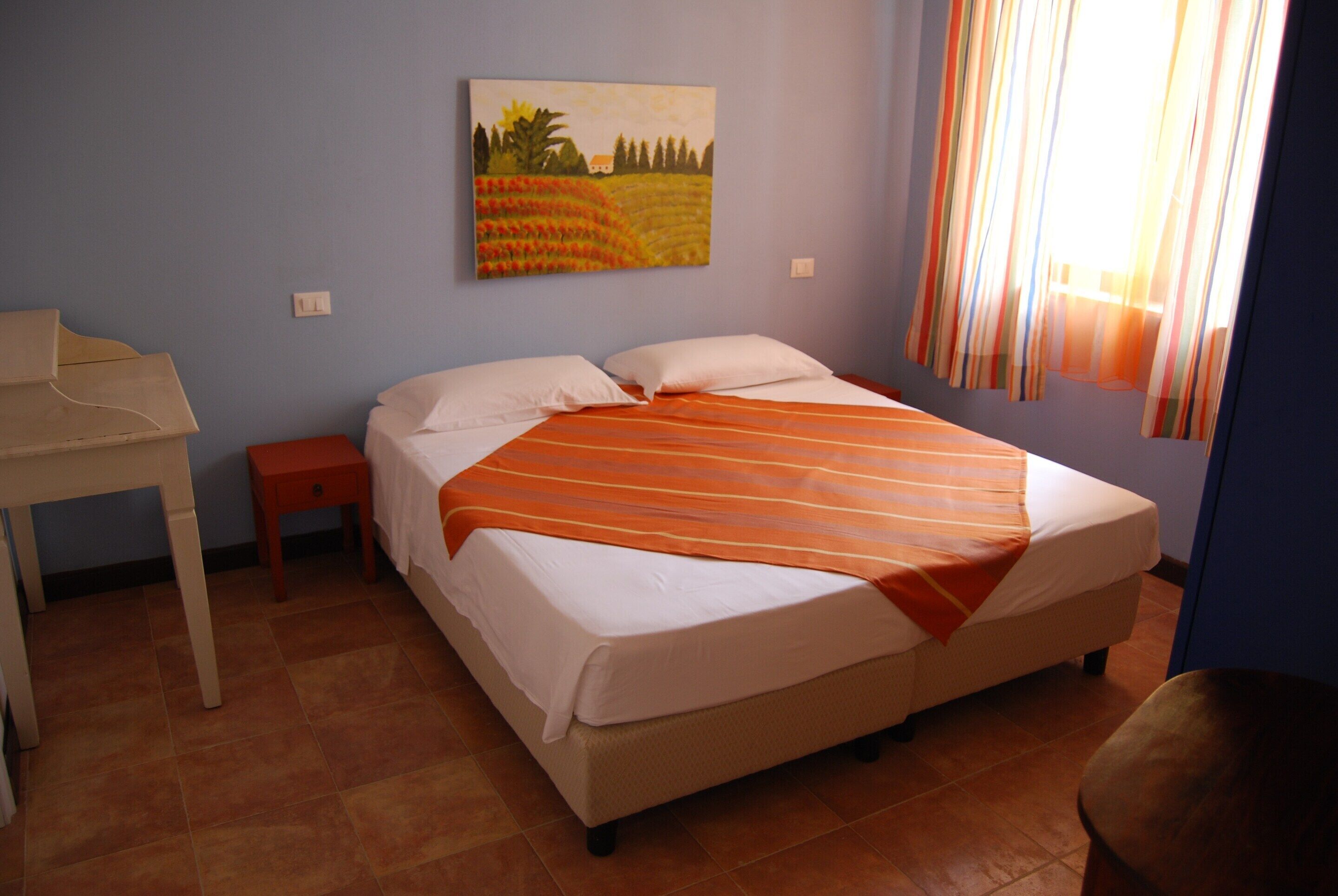 A bedroom with a bed, a desk, and a painting on the wall.