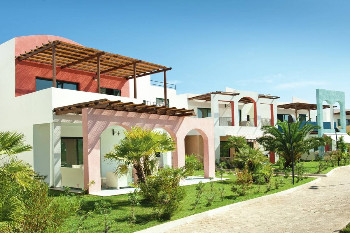 Een modern hotel met een overdekt terras, meerdere balkons en weelderige beplanting.