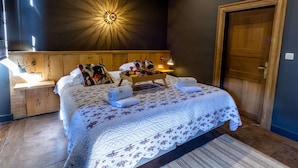 A bedroom with a wooden headboard, a bed with a floral quilt, a nightstand with a lamp, and a wall-mounted light fixture. - Splendid Castle in Perwez-haillot With Sun-loungers (Ohey)