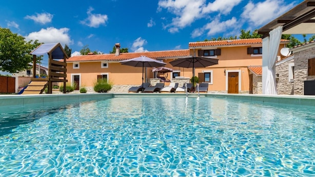 A clear swimming pool with lounge chairs and umbrellas, surrounded by buildings with a Mediterranean architectural style. - Charming Villa With Private Swimming Pool (Zminj)
