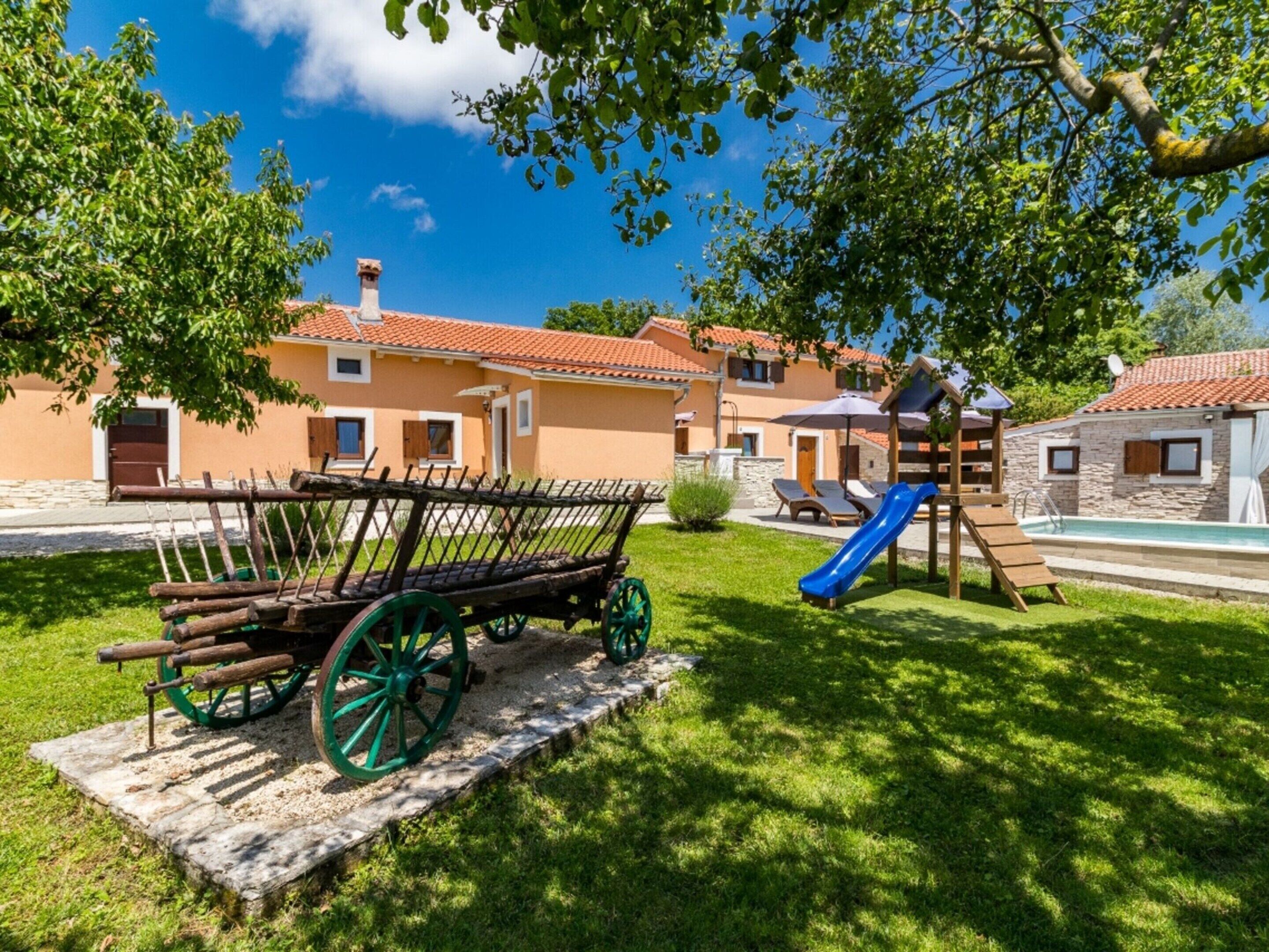 Ein Spielplatz mit Rutsche und Schaukeln, einem hölzernen Wagen und einem Poolbereich.