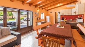 A cozy interior with a wooden ceiling, a dining area with a table and benches, a kitchen with white cabinets, and a view of a swimming pool outside. - Charming Villa With Private Swimming Pool (Zminj)