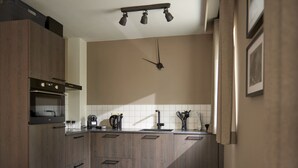 A modern kitchen with wooden cabinets, a built-in oven, a coffee maker, and a clock on the wall. - Apartment in Durbuy in a Wooded Holiday Park (Durbuy)