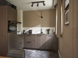 Una cocina moderna con armarios de madera, horno empotrado, cafetera y un reloj en la pared.