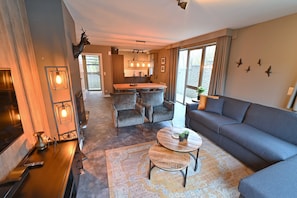 Un salon comprenant un canapé, une table basse, une cheminée, un téléviseur et un coin cuisine avec une table à manger et des chaises.