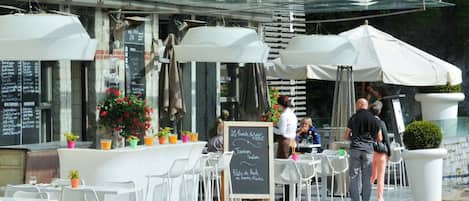 An outdoor cafe with white chairs and tables, a chalkboard menu, and potted plants.