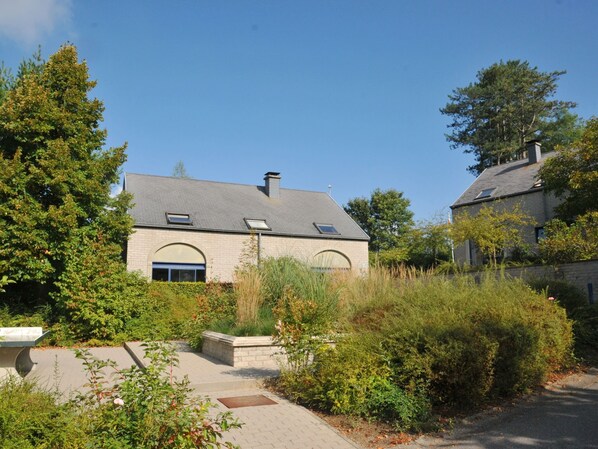 A two-story house with a sloped roof, a small attached garage, and a paved driveway. - Apartment in Durbuy in a Wooded Holiday Park (Durbuy)