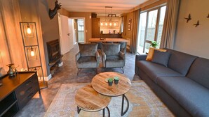 A modern living room with a sofa, two armchairs, a coffee table, and a fireplace. There is a kitchen in the background with a dining area. - Apartment in Durbuy in a Wooded Holiday Park (Durbuy)