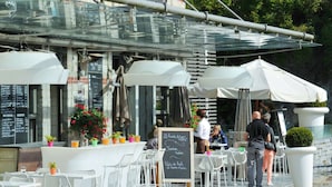 Een terras met witte stoelen en tafels, een krijtbord met de menukaart en plantenpotten.