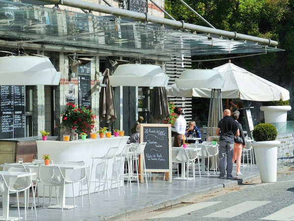 Een terras met witte stoelen en tafels, een krijtbord met de menukaart en potplanten.