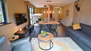 Een moderne woonkamer met een grijze bank, een salontafel met planten, een eethoek met een houten tafel, en een tv aan de muur bevestigd.
