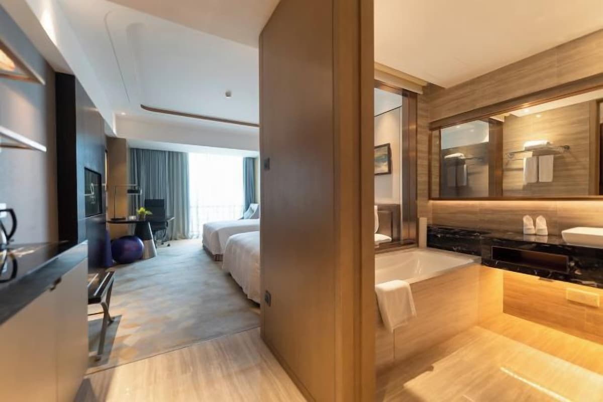 A modern hotel room with a large bed, a separate bathroom with a bathtub, and a kitchenette area.