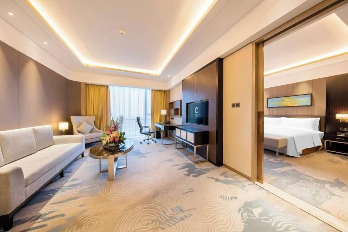 A hotel room with a sofa, a coffee table, a TV, a desk, and a bed.