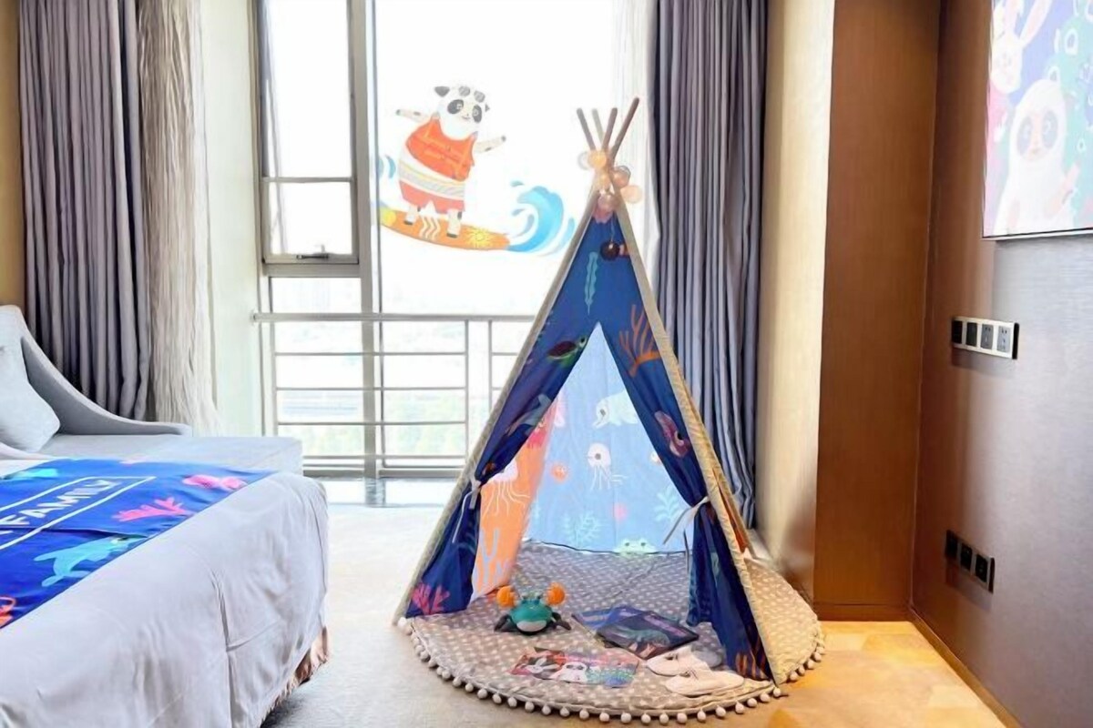 Camera d'albergo con un letto, una finestra con tende, una TV a parete e un tipì decorato con un panda.