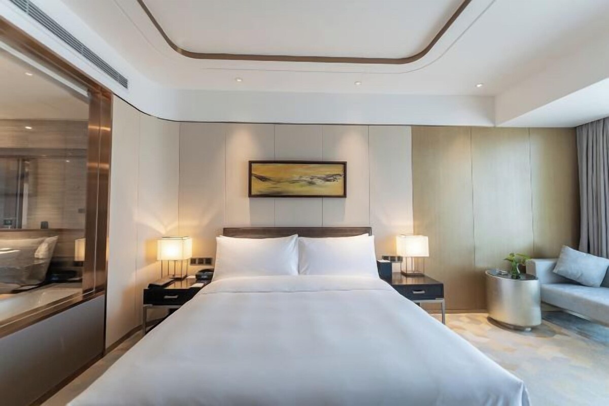 Una camera d'albergo moderna con un letto grande, due comodini con lampade, un divano e un quadro appeso al muro.