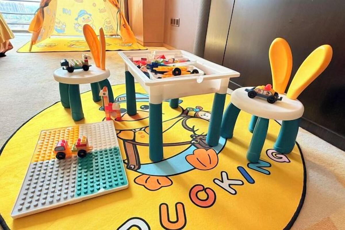 Un'area giochi per bambini con un tavolo LEGO, macchinine giocattolo e un tappetino con un disegno di anatra.