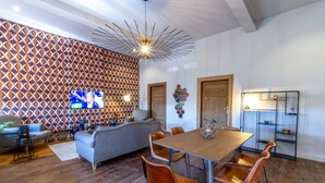 A modern living room with a patterned wall, a large TV, a dining table with chairs, and a decorative shelf.