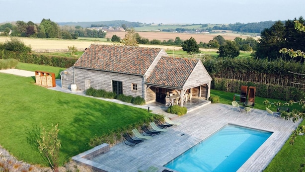 A wooden house with a swimming pool, a patio with lounge chairs, and a view of the countryside.