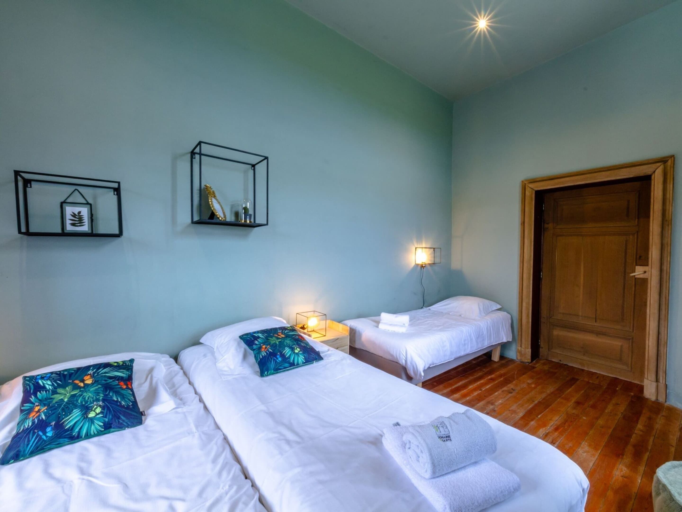 A hotel room with two beds, a wooden door, and wall-mounted light fixtures.