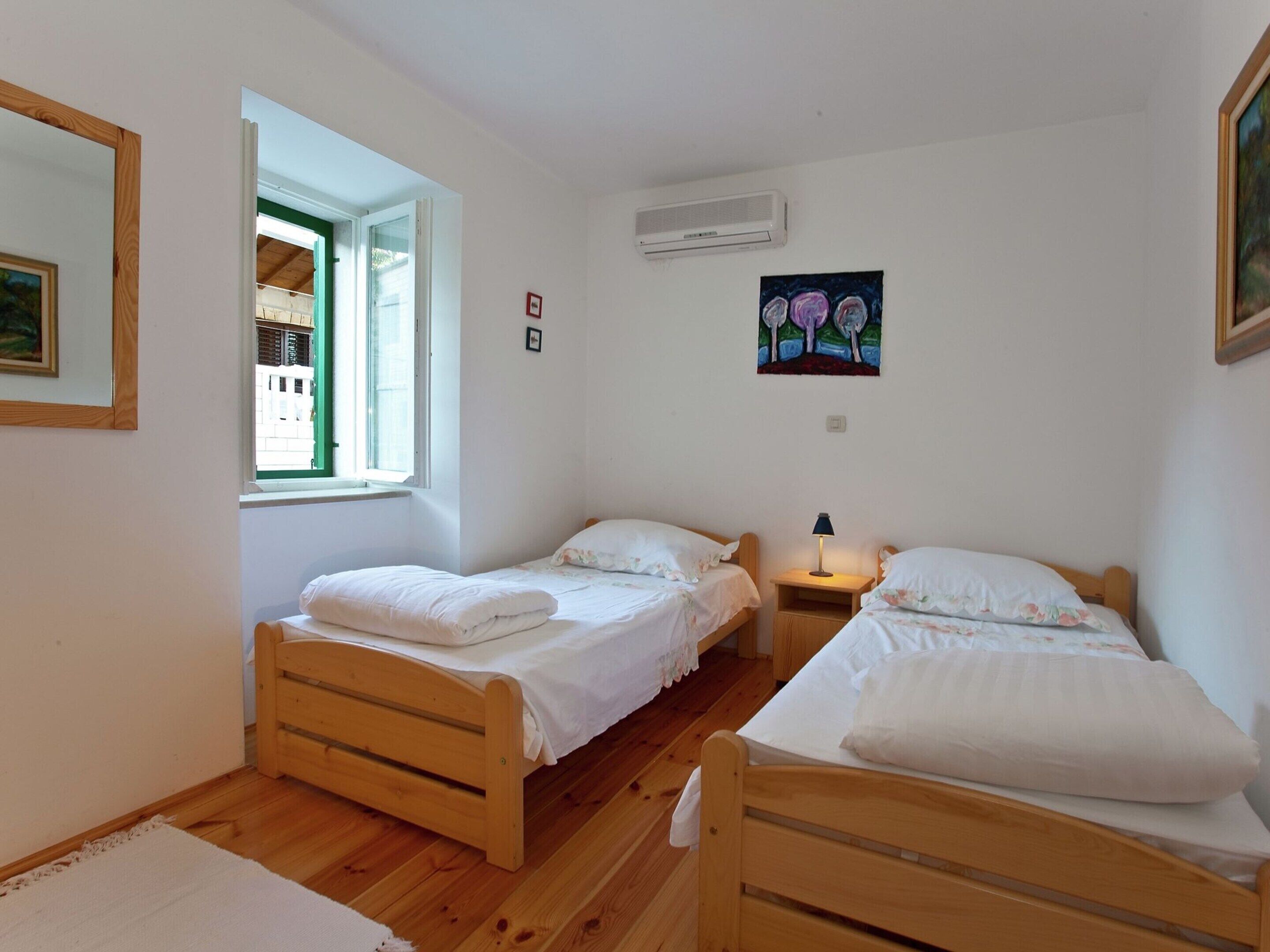 Una habitación pequeña y ordenada con dos camas de madera, un ventanal y un cuadro en la pared.
