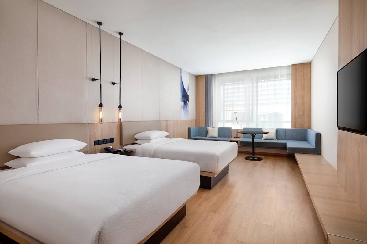 Habitación de hotel con dos camas, un sofá, un televisor y una ventana con vistas.
